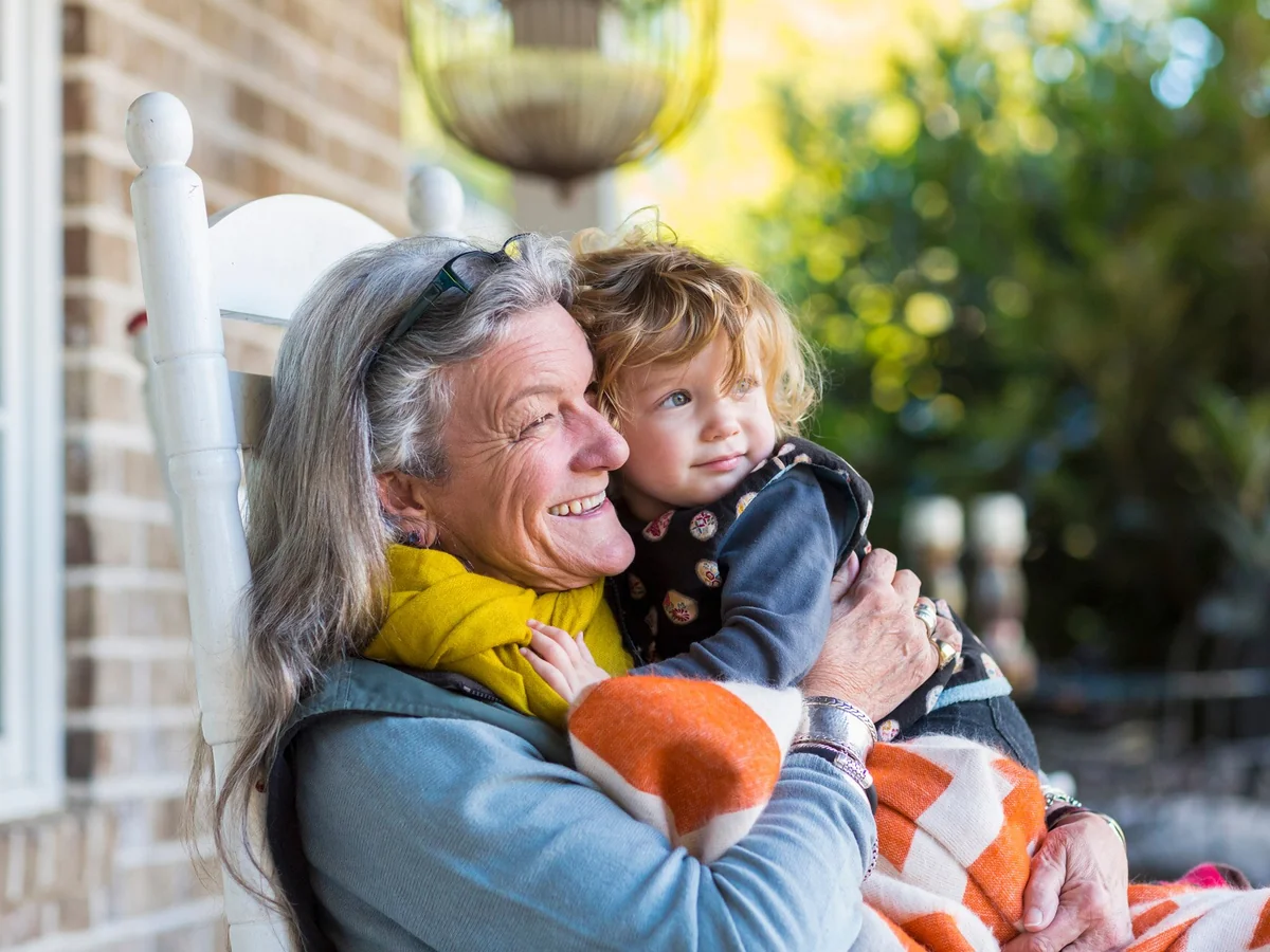 Smiling grandmother holding her grandchild on a sunny porch